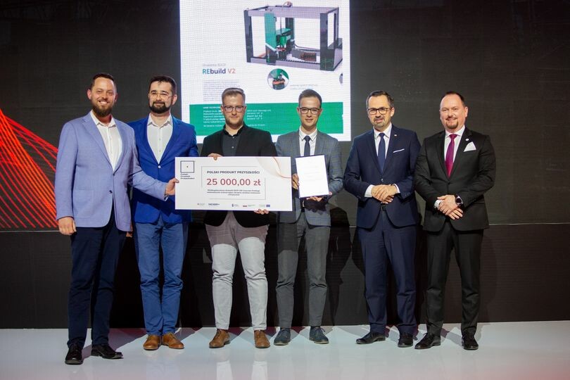 Grupa ludzi w średnim wieku pozuje do zdjęcia na scenie trzymające w rękach dużych czek