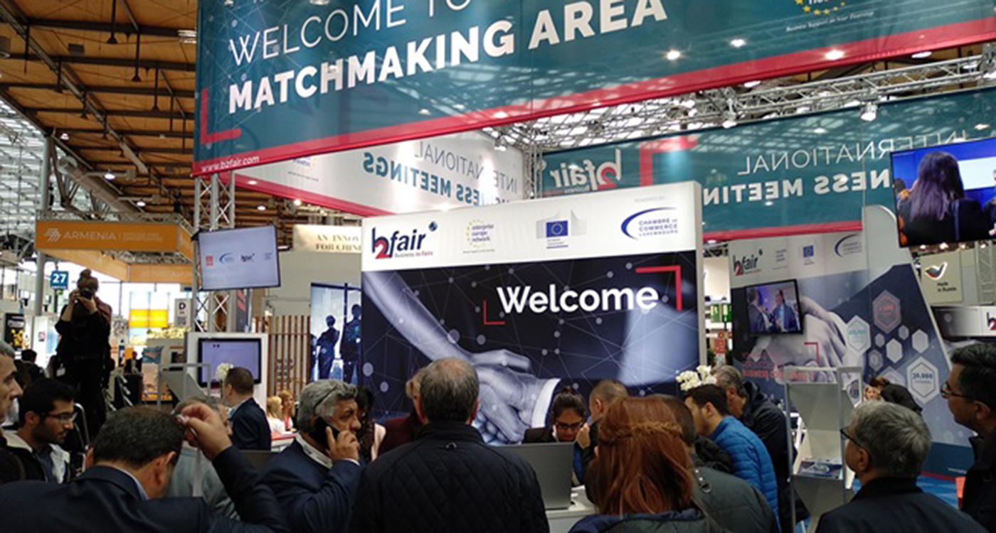 Grupa ludzi w różnym wieku stoi zgromadzona w hali służącej jako przestrzeń do spotkań biznesowych