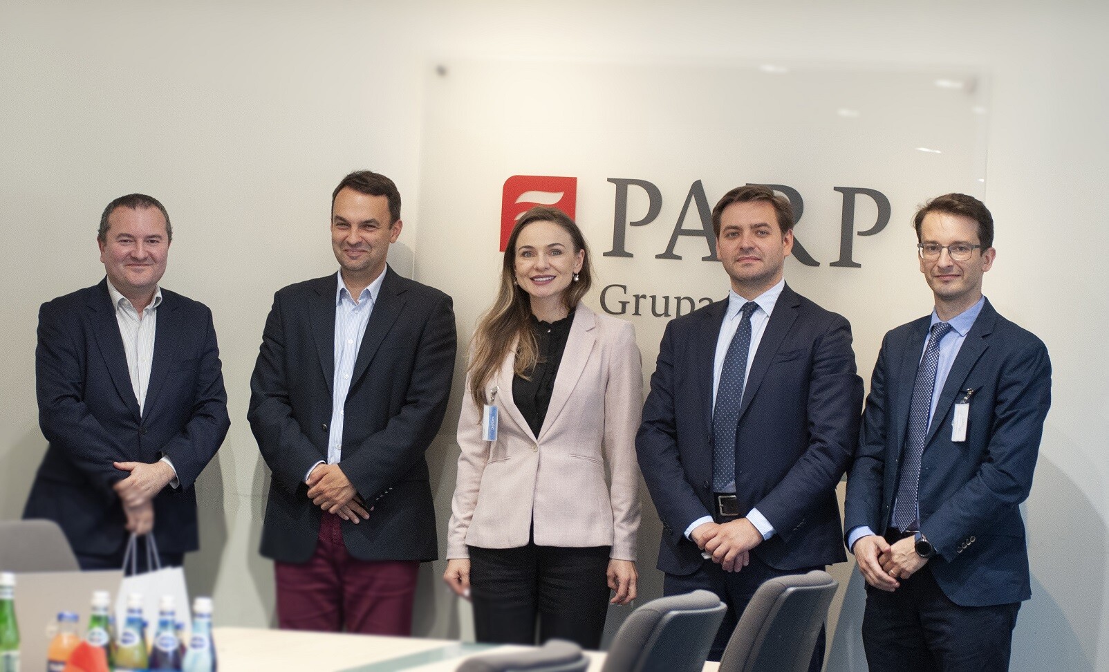 grupa ludzi w średnim wieku stoi w sali i patrzy się w obiektyw