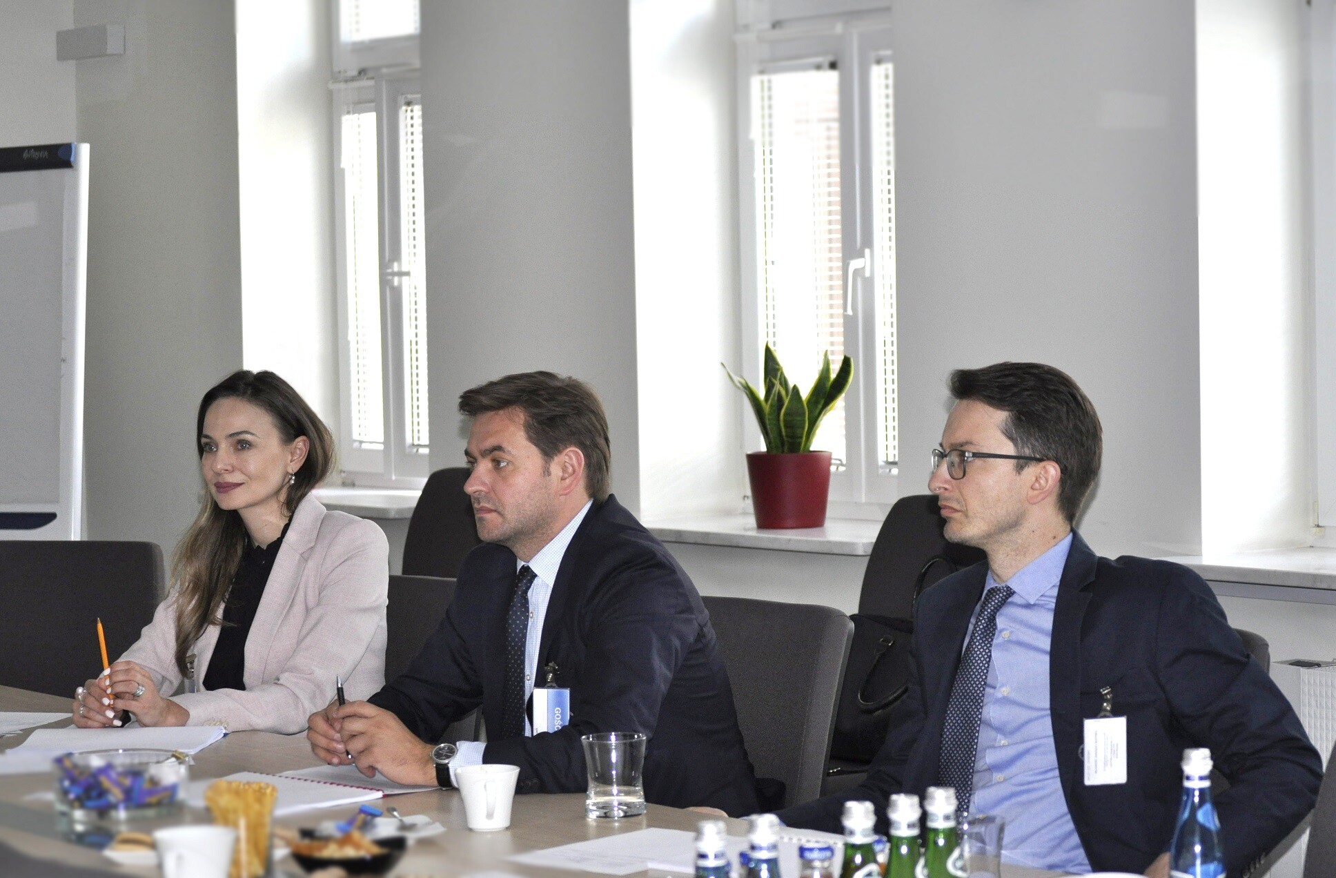 Dwóch mężczyzn i kobieta ubrani w stroje biznesowe siedzi przy stole