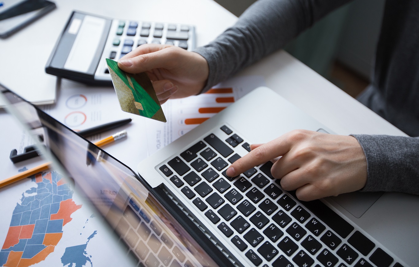 Zbliżenie na dłoń trzymającą w ręce kartę płatniczą na tle klawiatury laptopa