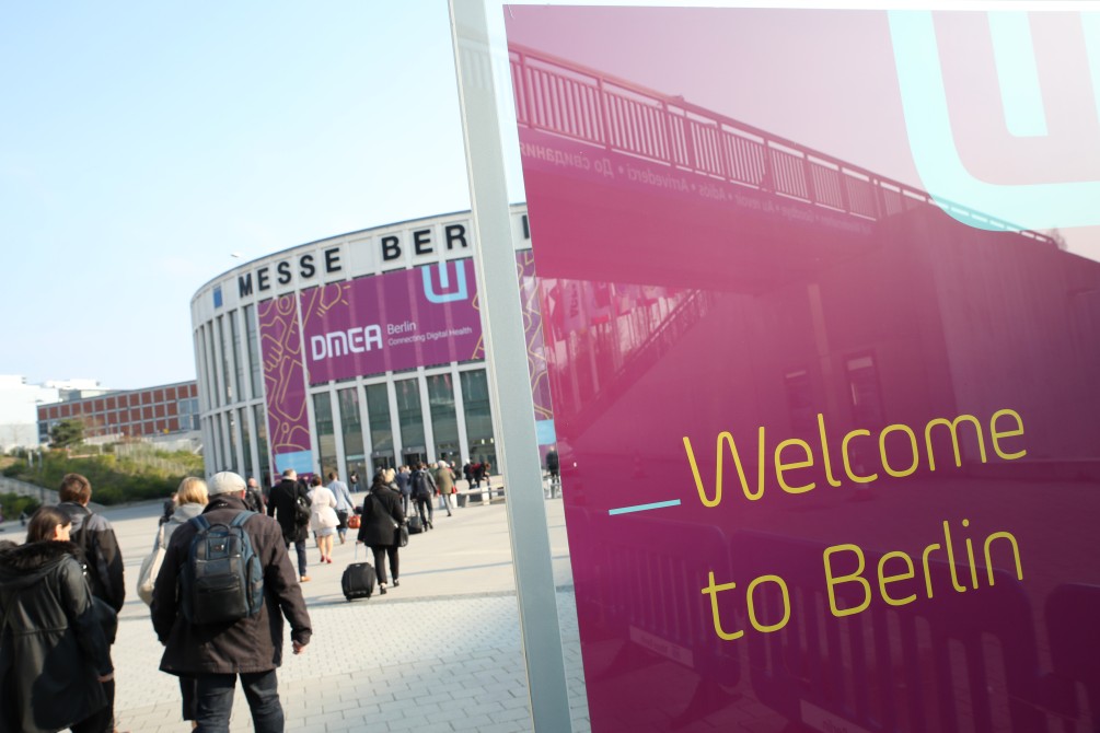 Na pierwszym planie czerwona flaga z anglojęzycznym napisem Welcome to Berlin. W głębi widać niski...