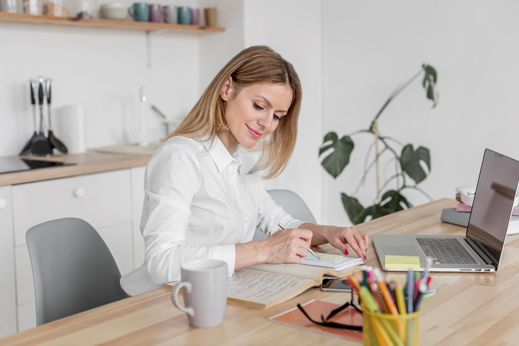 Na zdjęciu widać młodą kobietę, ubraną w białą koszulę. Kobieta siedzi przy dużym, jasnym...