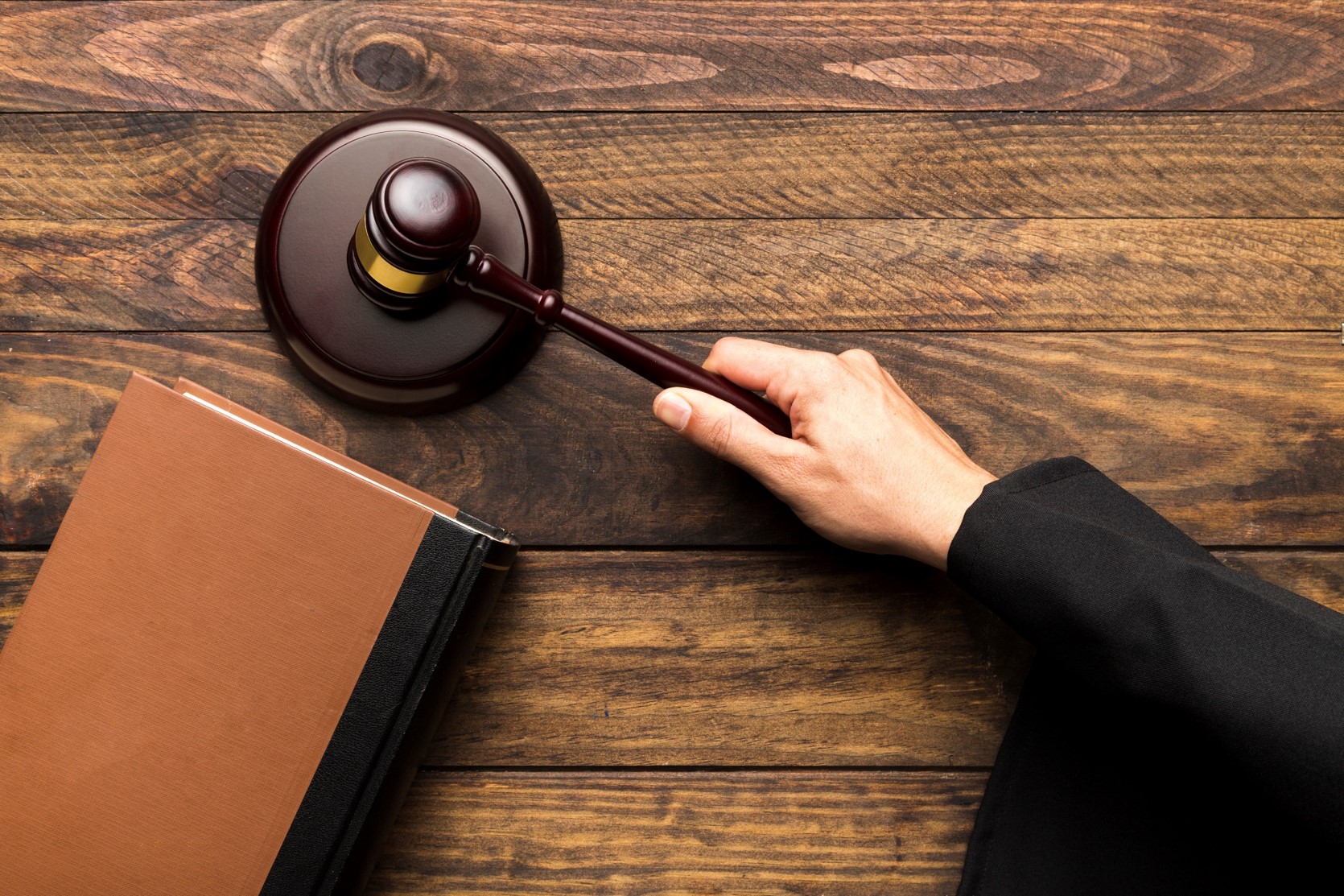 widok z góry na stół sędziego. Widać jego rękę trzymającą młotek i uderzając w drewnianą kołatkę, postawioną na biurku