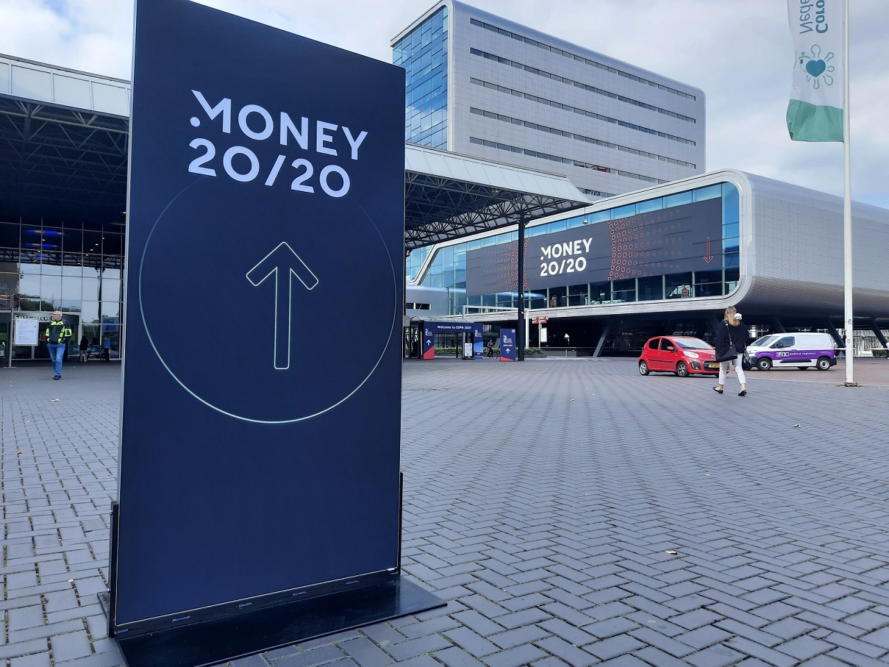 Grafika przedstawiająca tablicę z w przestrzeni miejskiej z napisem "Money20/20" na tle...