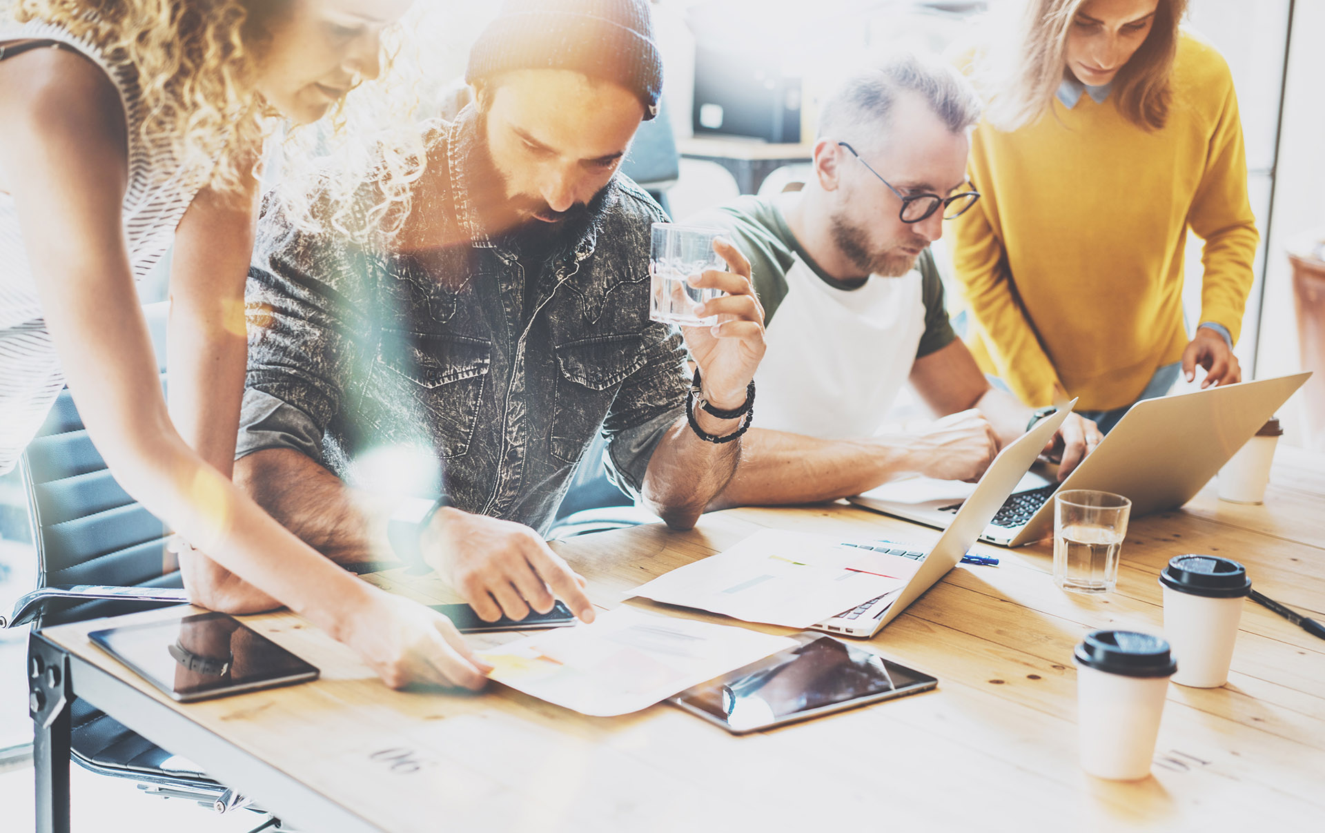 Młodzi ludzie siedzą przy wspólnie przy dużym długim biurku i patrzą w papiery