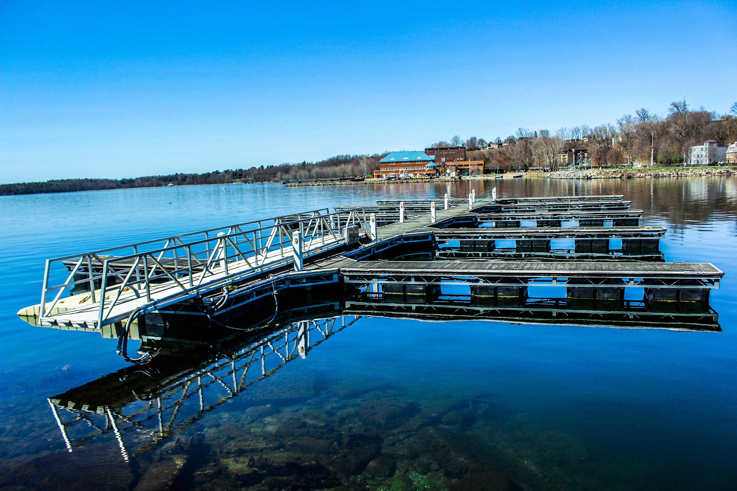 Widok na "pływający" pomost na tle brzegu jeziora. Zdjęcie zrobione w dzień, jesienią. Niebo bezchmurne.