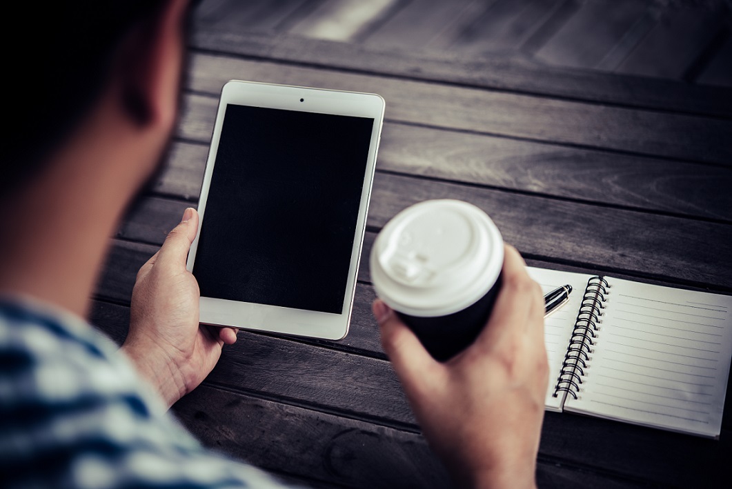 Młody mężczyzna siedzi przy stoliku, trzyma w ręku zielony kubek, z zakrytym wieczkiem i patrzy...