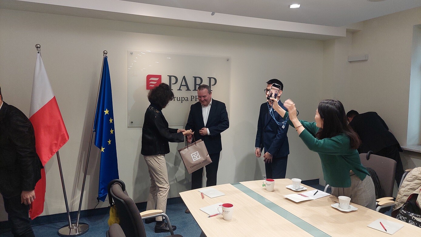 Mężczyzna i kobieta pozują do zdjęcia. Obok flagi Polski i Unii Europejskiej oraz ścianka z napisem PARP