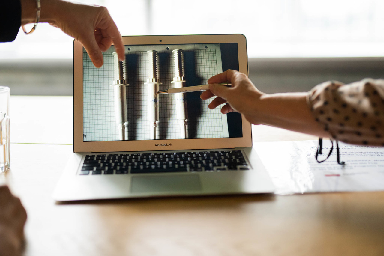 Laptop stoi na biurku, wokół ręce, które wskazują na ekran.
