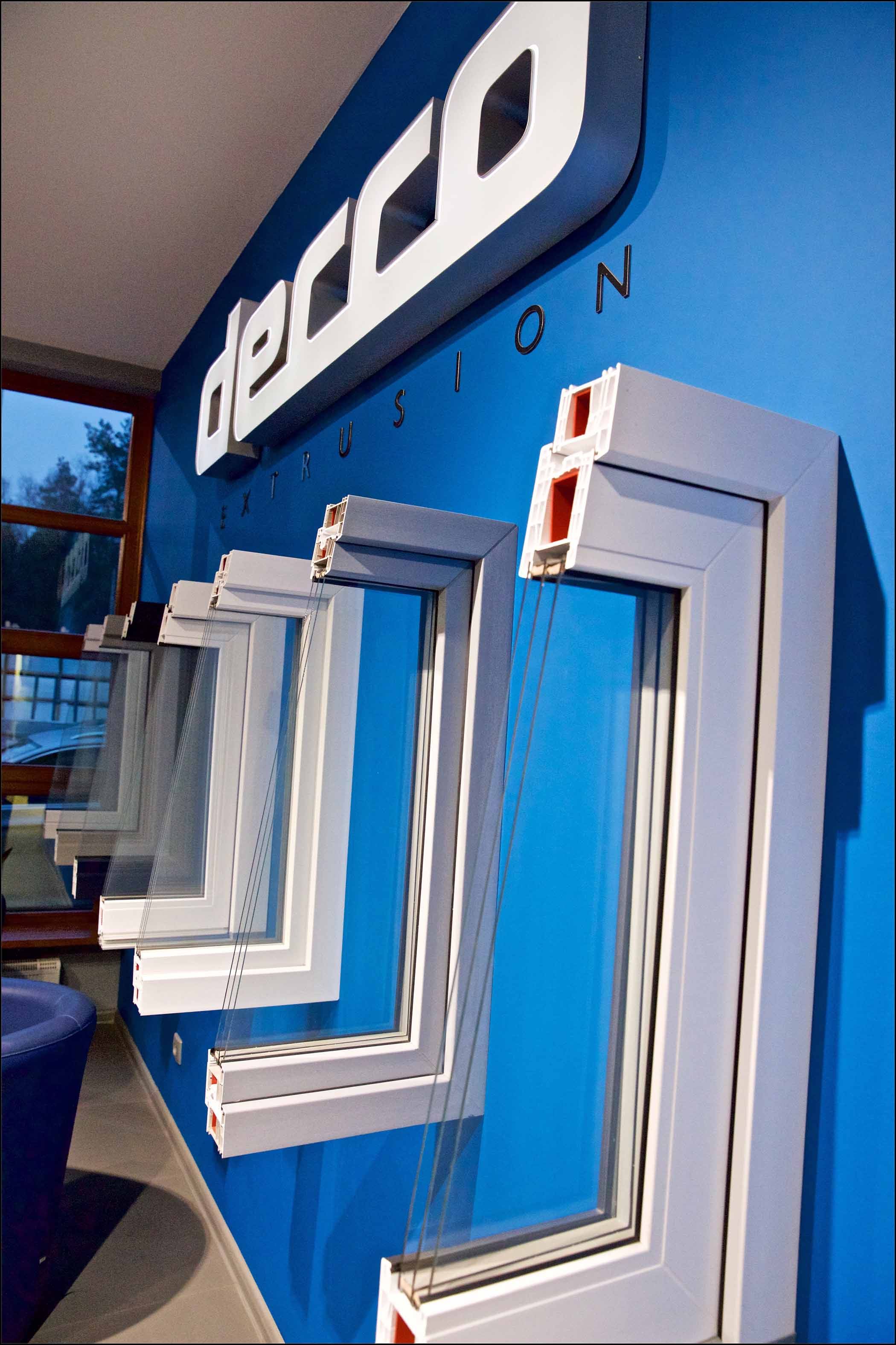 Nazwa firmy Decco umieszczona na ścianie wraz z ramą okna PVC