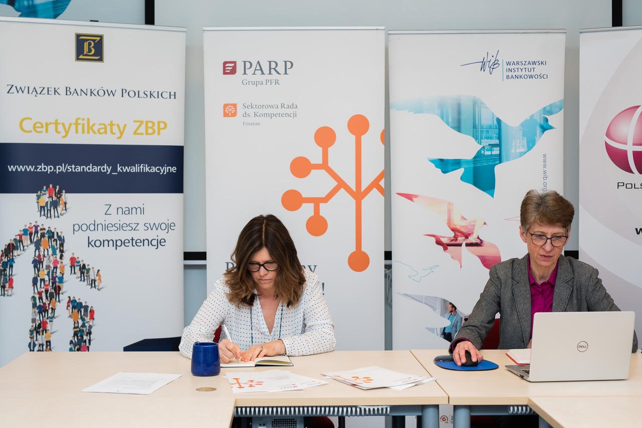 Dwie kobiety siedzą na tle rollupów